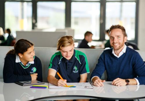 Male teacher with high school students at desk