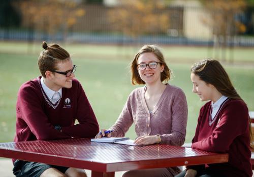 Female teacher sitting with high school students outdoors