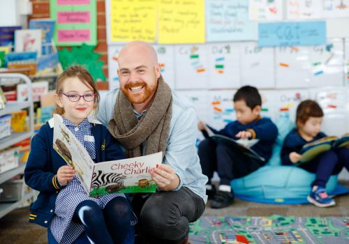 Male teacher with primary school student reading book