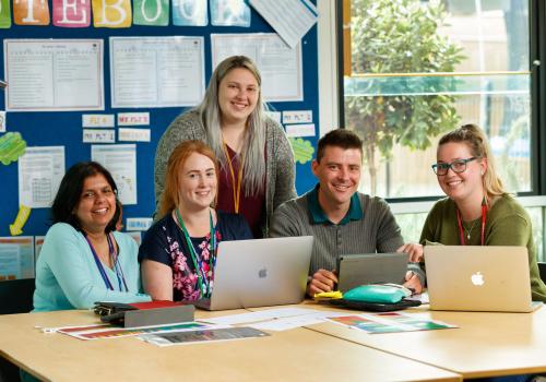 Five adults sitting in front of their laptops at a desk. 