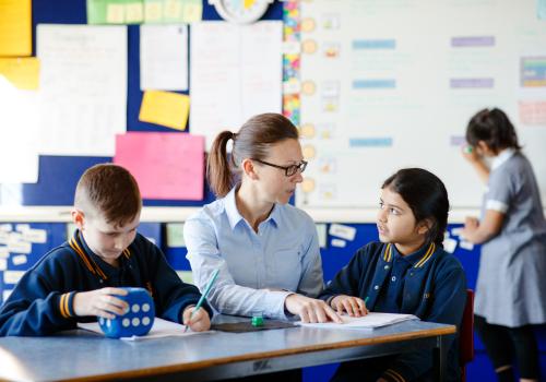 Teacher sitting between two students at desk. 