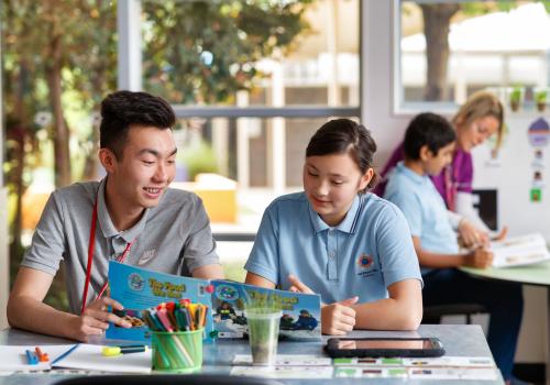 Male teacher sitting with student reading a book. 