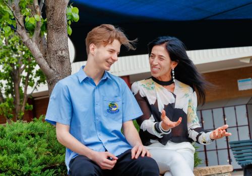 Female teacher sitting with secondary student outdoors. 