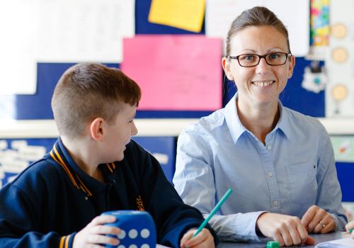 Teacher seated next to a primary school student holding a dice