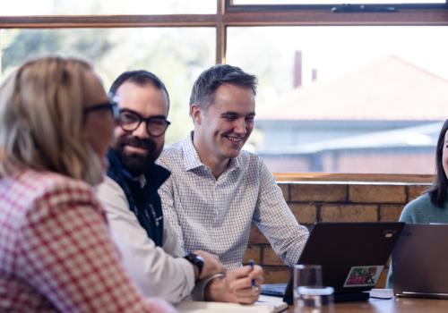 Teachers at a school sit together at a table smiling
