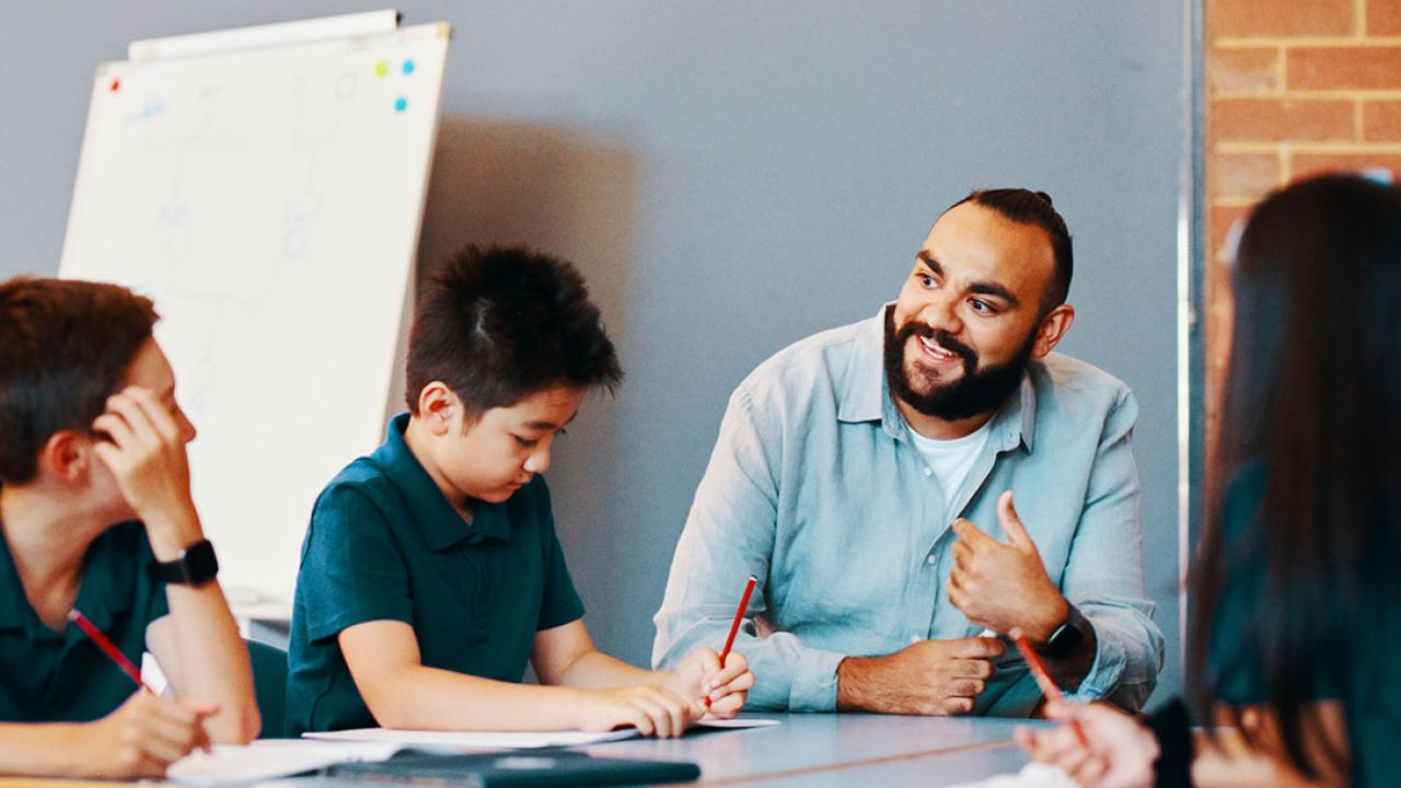Teacher seated and in discussion with primary school students at their desk