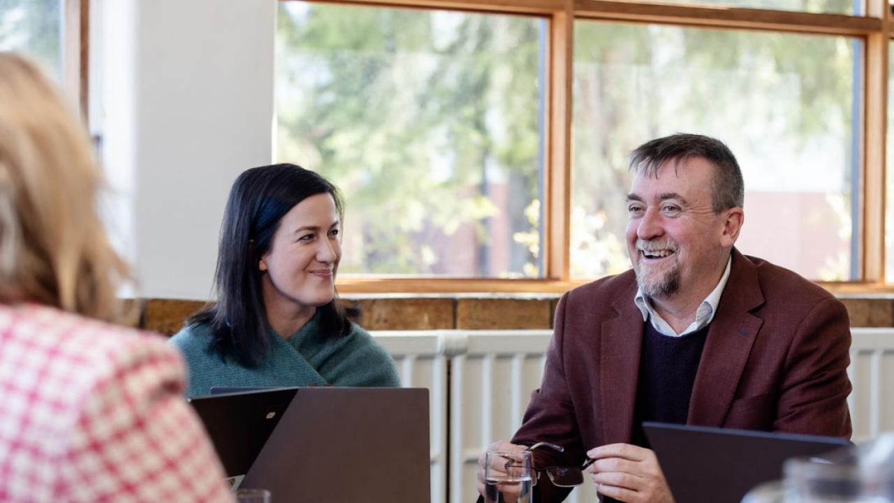 2 teachers seated at table with a laptop and smiling