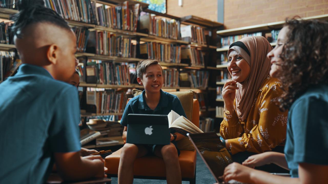 Students with ipad and laptop sitting with teacher in the library