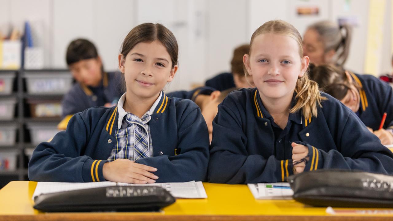2 primary school students sitting at desk with their notebook and pencil cases