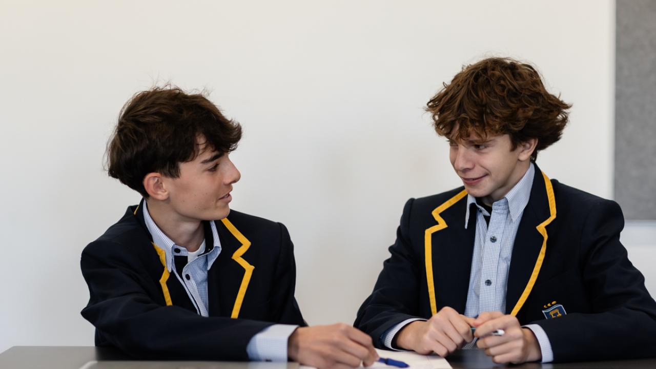 2 secondary students seated at table in discussion