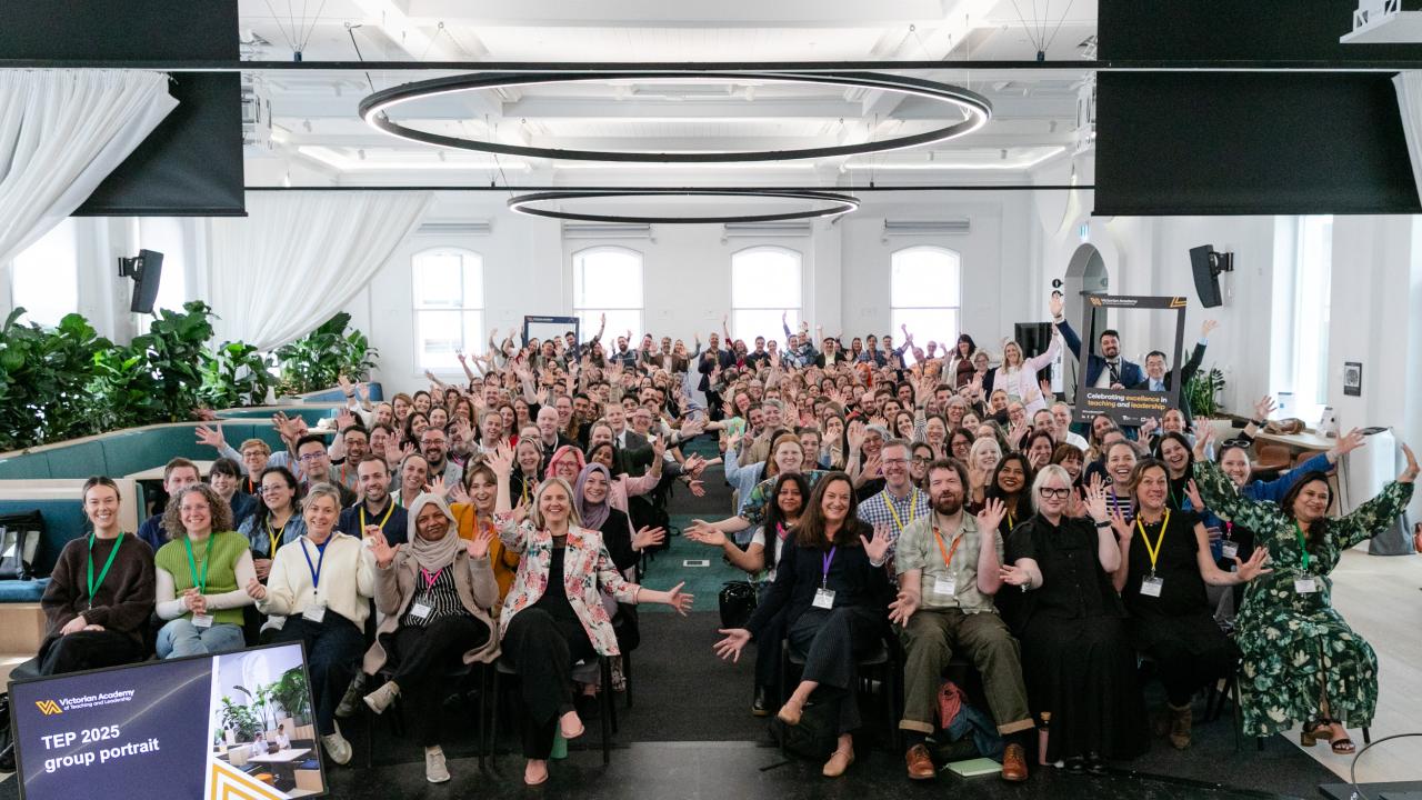 Full room of Teaching Excellence Program graduates seated in audience and waving