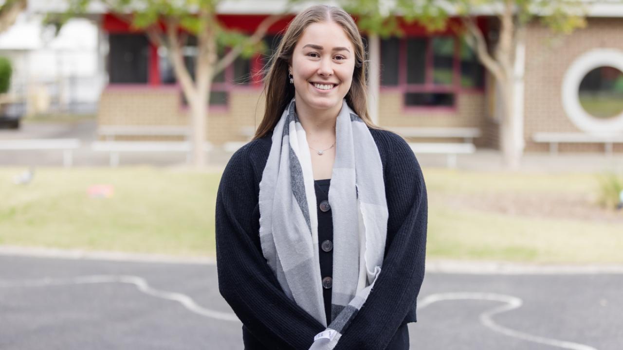 Teacher smiling and standing outside on school grounds