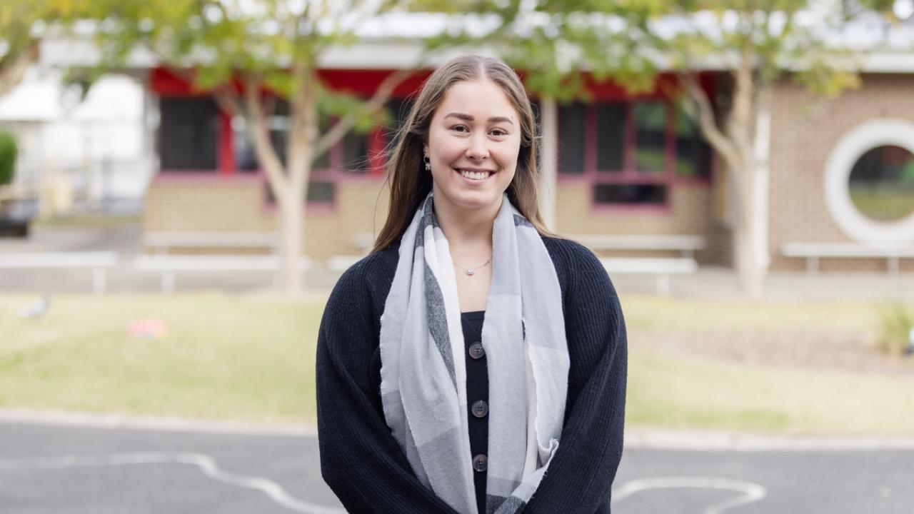 Teacher smiling and standing outside on school grounds