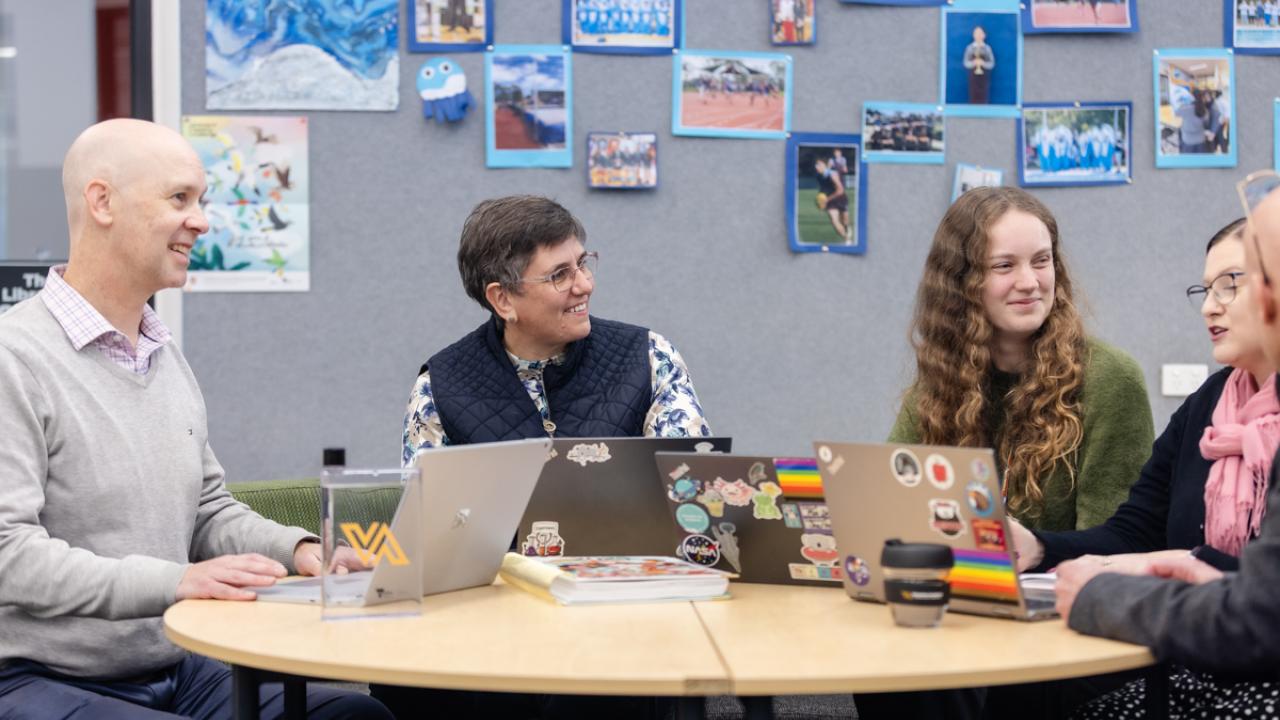 A group of teachers seated around table with laptops in discussion