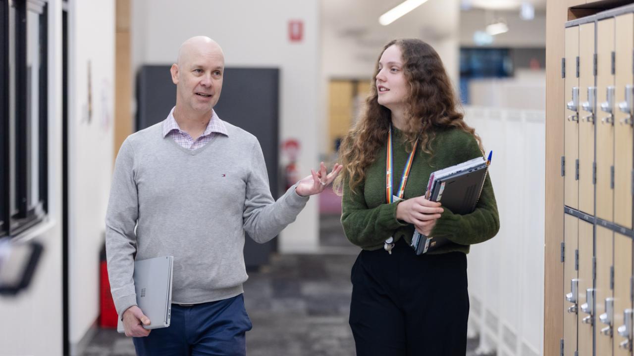2 teachers with books in hand walking in school corridor