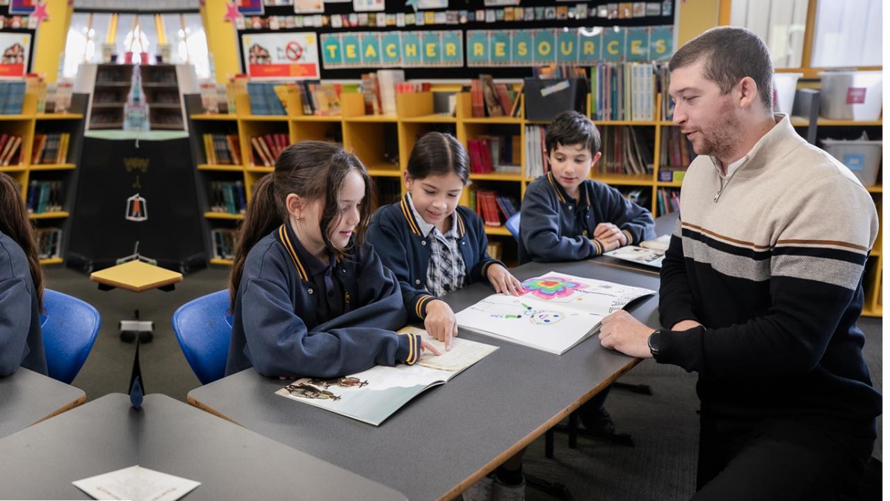 Image to teacher with primary school students sitting at table.
