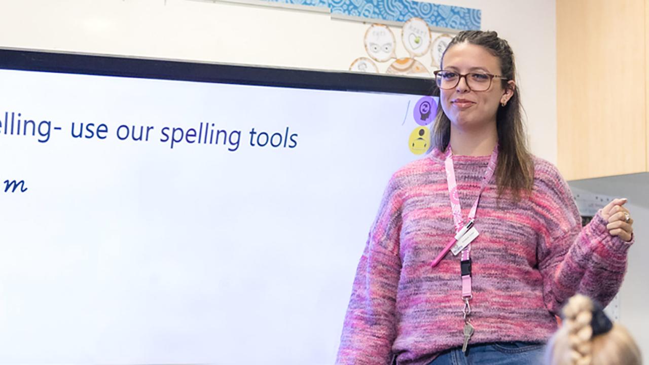 Literacy teacher at the white board with the instruction written on the board as spelling - using our tools. 