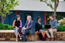 Group of 4 adults sitting outside talking in pairs. 