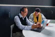 Adults sitting around a table looking at laptop. 