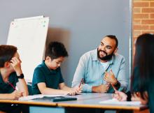 Teacher seated and in discussion with primary school students at their desk