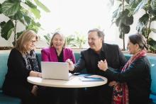 Team of 4 are working together at table focused on a laptop