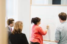A group of 4 people collaborating together with one participant writing on a whiteboard