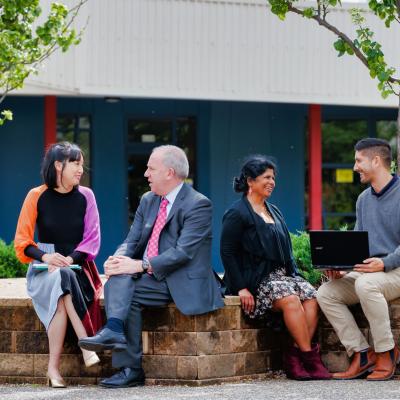 Group of 4 adults sitting outside talking in pairs. 