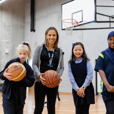 Teacher with primary school students holding basketballs inside school gym building