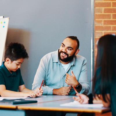 Teacher seated and in discussion with primary school students at their desk