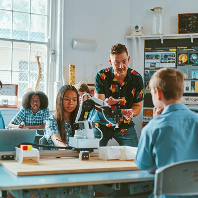 Teacher speaking to high school students at desk in classroom  