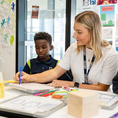 Teacher seated with 2 primary school students at their desk writing on a mini whiteboard