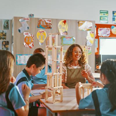 Teacher seated with primary school students at their desk building structures with wooden blocks 