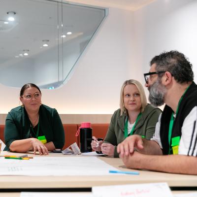 5 participants seated around table in discussion with paper and textas