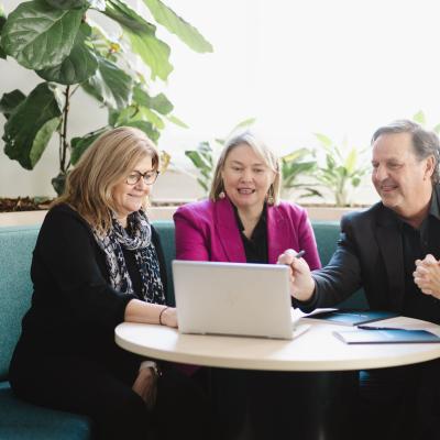 Team of 4 are working together at table focused on a laptop