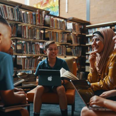 Students with ipad and laptop sitting with teacher in the library