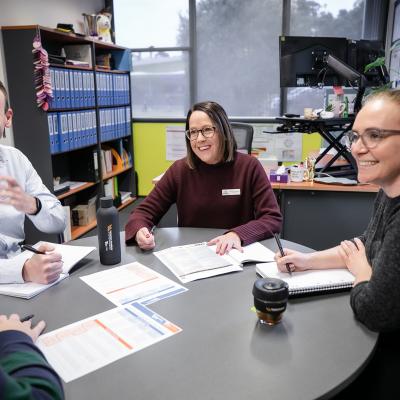 4 school leaders are seated around table in discussion and smiling