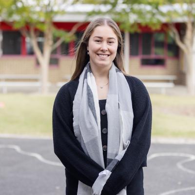 Teacher smiling and standing outside on school grounds