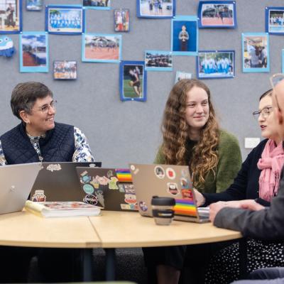 A group of teachers seated around table with laptops in discussion