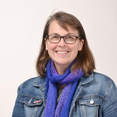 Headshot of Dr Peta White. She is wearing a denim jacket and scarf around her neck.